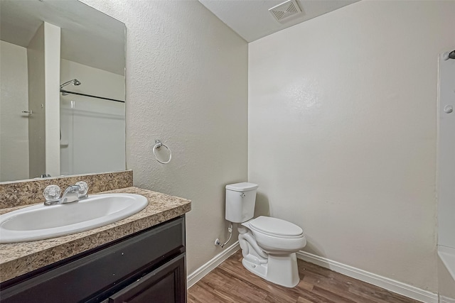 bathroom with toilet, wood finished floors, vanity, visible vents, and a shower