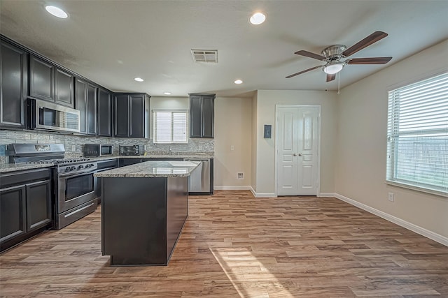 kitchen with stainless steel appliances, visible vents, light wood-style floors, decorative backsplash, and light stone countertops