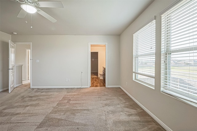 unfurnished bedroom featuring light carpet, a walk in closet, a ceiling fan, and baseboards