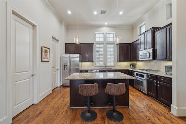 kitchen featuring appliances with stainless steel finishes, a center island, crown molding, and dark brown cabinetry