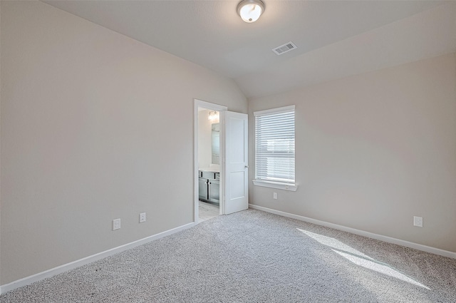 unfurnished bedroom featuring light colored carpet, visible vents, vaulted ceiling, ensuite bath, and baseboards