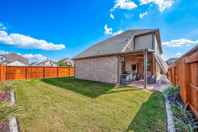 rear view of property featuring a fenced backyard, brick siding, a shingled roof, a yard, and a patio area