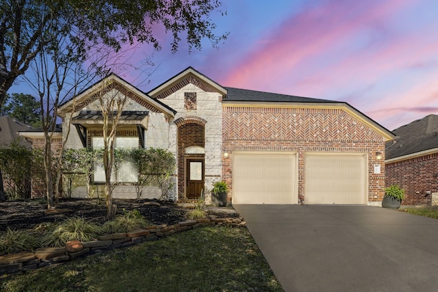 french country home with brick siding, roof with shingles, a garage, stone siding, and driveway