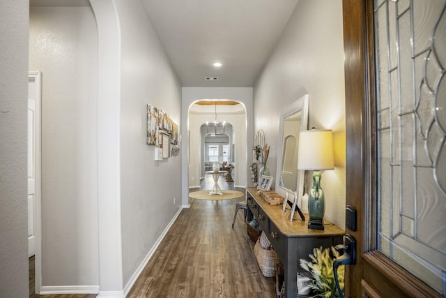 hallway with arched walkways, wood finished floors, and baseboards