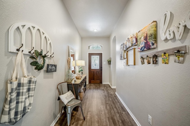 doorway with arched walkways, dark wood-type flooring, and baseboards