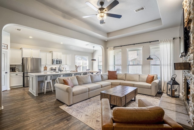 living room featuring dark wood-style floors, plenty of natural light, visible vents, and a raised ceiling