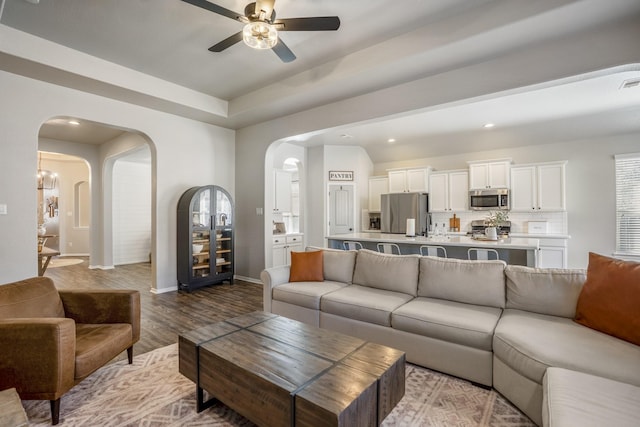 living area with arched walkways, ceiling fan, wood finished floors, and baseboards