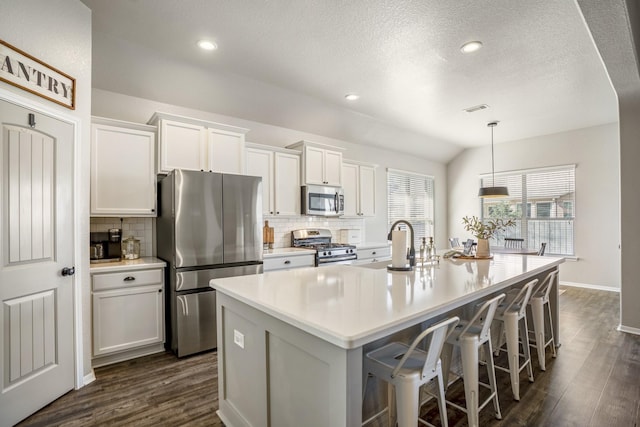 kitchen with visible vents, dark wood-style floors, a kitchen island with sink, stainless steel appliances, and light countertops