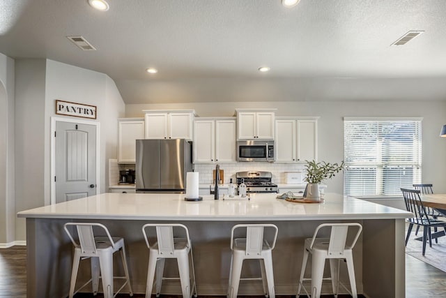 kitchen featuring a large island, visible vents, backsplash, appliances with stainless steel finishes, and white cabinetry