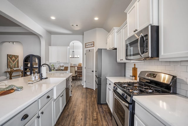 kitchen with white cabinetry, arched walkways, stainless steel appliances, and light countertops