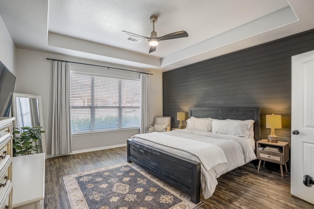 bedroom with wood walls, wood finished floors, visible vents, baseboards, and a tray ceiling