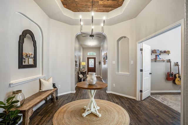 foyer with arched walkways, wood finished floors, a raised ceiling, and baseboards