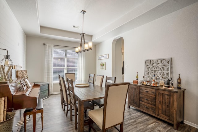 dining area featuring arched walkways, a tray ceiling, dark wood-style flooring, and visible vents