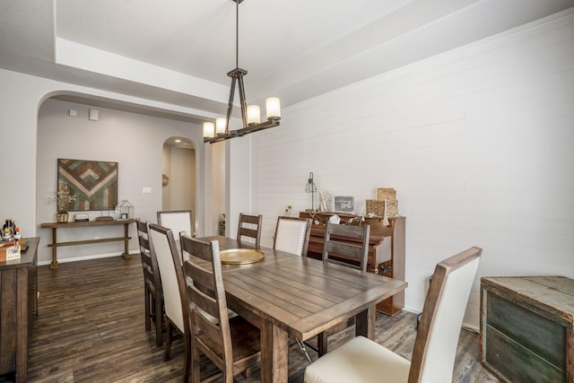 dining space featuring arched walkways, dark wood-style flooring, a tray ceiling, a chandelier, and baseboards