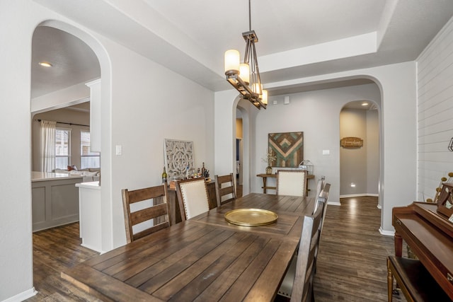 dining room featuring dark wood-style floors, baseboards, arched walkways, and a raised ceiling