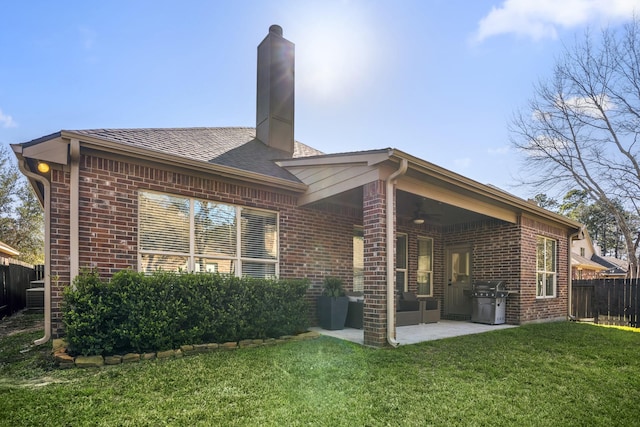 rear view of house featuring brick siding, a chimney, a lawn, ceiling fan, and fence