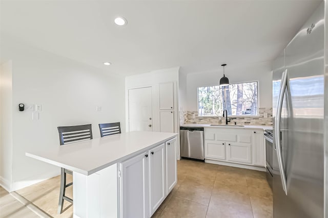 kitchen featuring a sink, white cabinets, light countertops, appliances with stainless steel finishes, and decorative backsplash