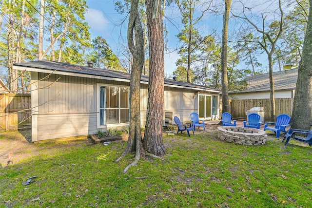 back of property featuring a fire pit, a lawn, and fence