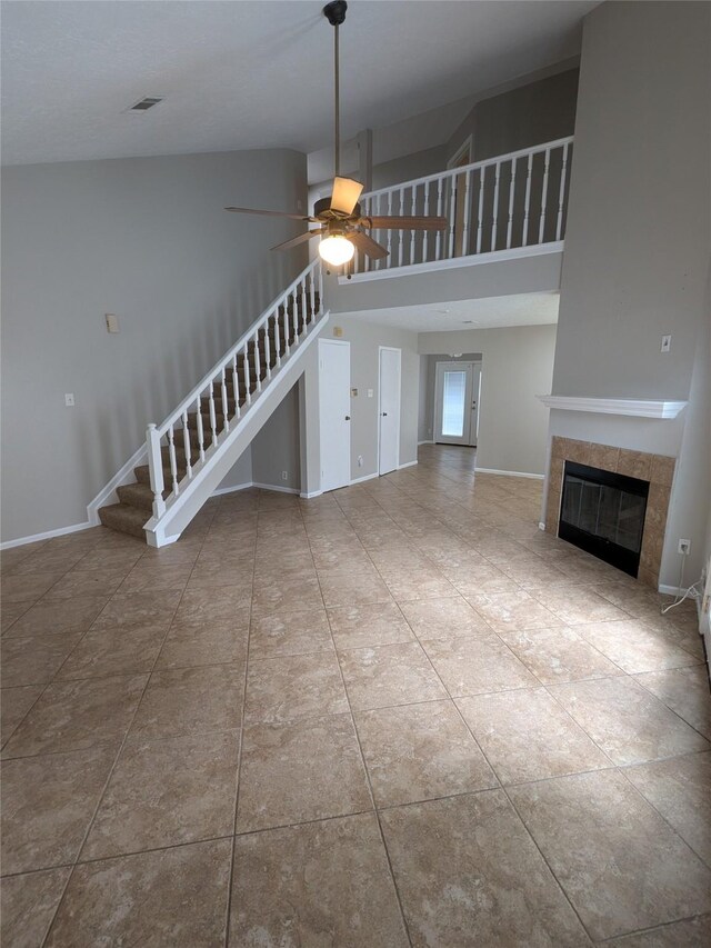 unfurnished living room featuring visible vents, a towering ceiling, stairs, baseboards, and a tiled fireplace