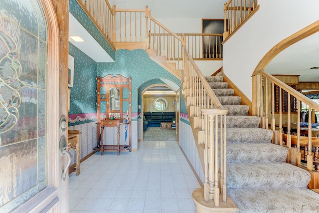 stairs with arched walkways, tile patterned flooring, and wallpapered walls