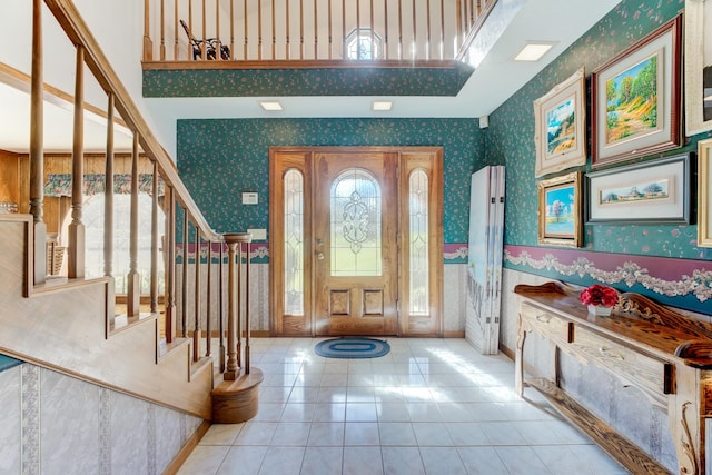 tiled foyer featuring stairs, a high ceiling, baseboards, and wallpapered walls