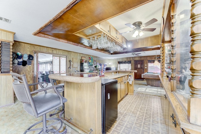 kitchen with wooden walls, visible vents, ceiling fan, a kitchen island, and light countertops