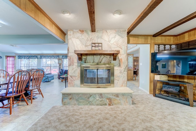 living area featuring carpet floors, beam ceiling, a fireplace, wood walls, and baseboards