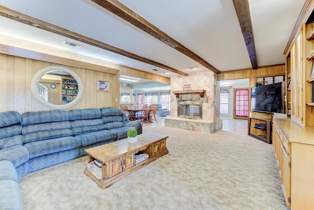 carpeted living room featuring a stone fireplace, beamed ceiling, visible vents, and wooden walls