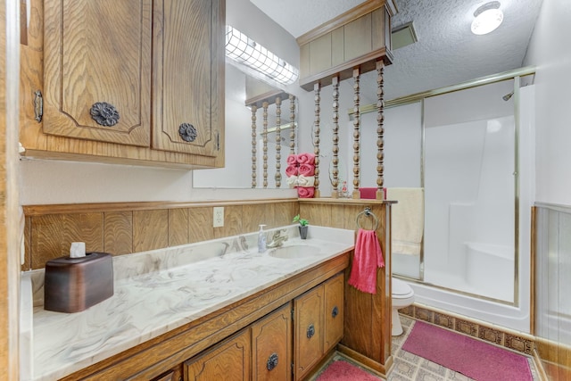 full bathroom with toilet, vanity, a textured ceiling, and a shower with shower door