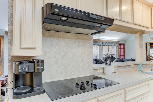 kitchen featuring black electric stovetop, light countertops, cream cabinetry, under cabinet range hood, and a sink