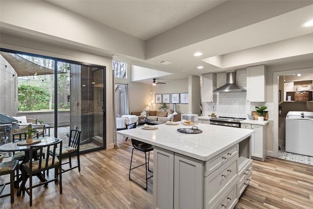 kitchen featuring washer / clothes dryer, electric range, wall chimney exhaust hood, and light wood finished floors