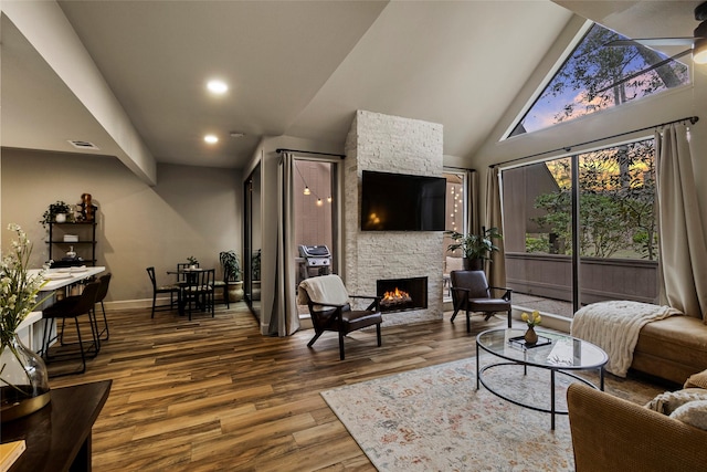 living room with baseboards, visible vents, wood finished floors, a stone fireplace, and high vaulted ceiling