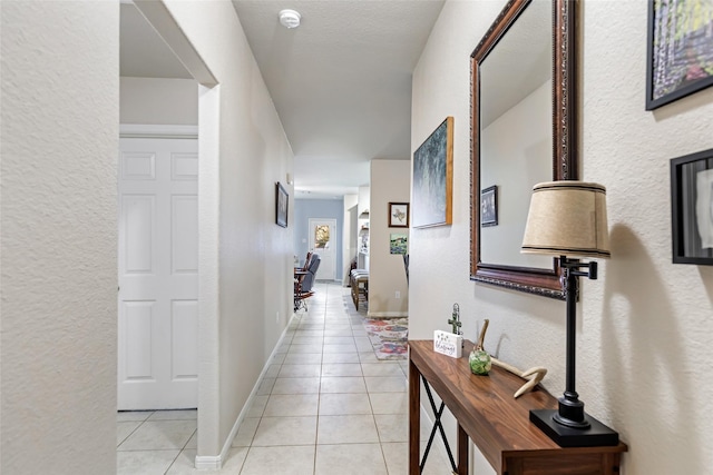 corridor with a textured wall, baseboards, and light tile patterned floors