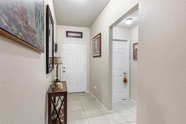 hall featuring a textured wall, baseboards, and light tile patterned flooring