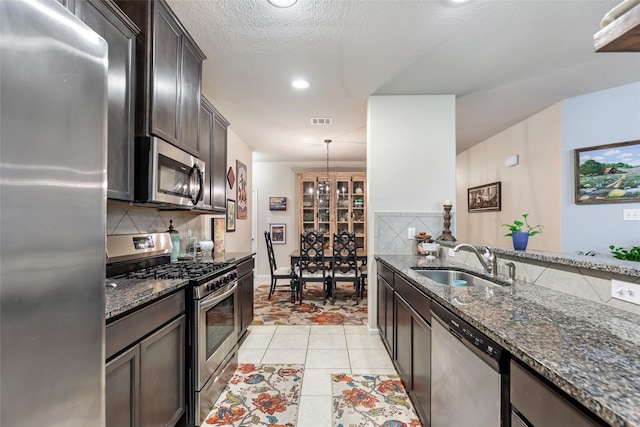 kitchen with appliances with stainless steel finishes, dark stone counters, a sink, and decorative backsplash