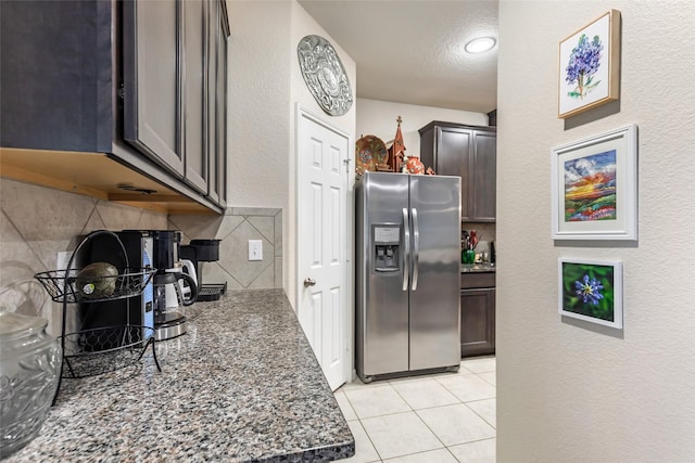 kitchen featuring tasteful backsplash, dark stone counters, stainless steel fridge, and light tile patterned flooring