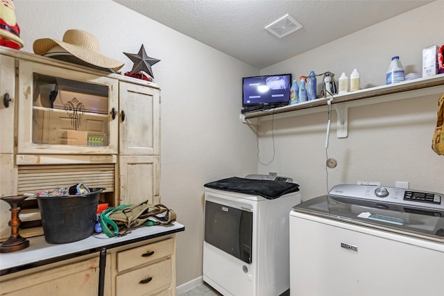 laundry area with a textured ceiling, separate washer and dryer, cabinet space, and visible vents