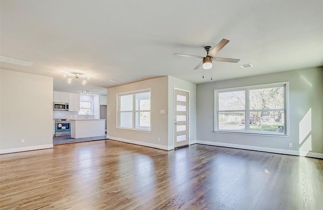 unfurnished living room featuring a sink, wood finished floors, a ceiling fan, and baseboards