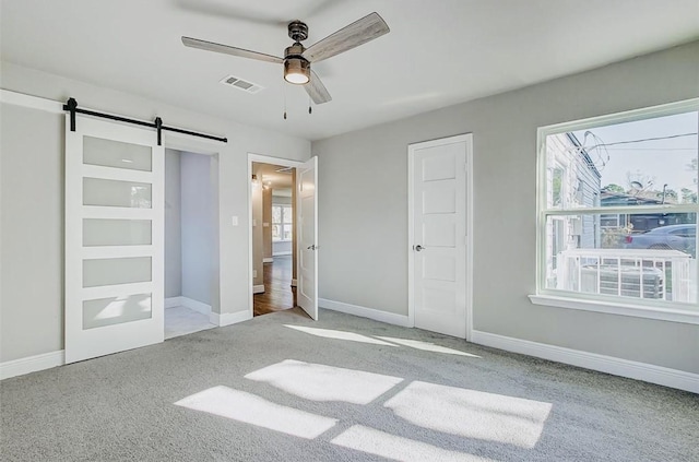 unfurnished bedroom featuring carpet floors, a barn door, visible vents, and baseboards