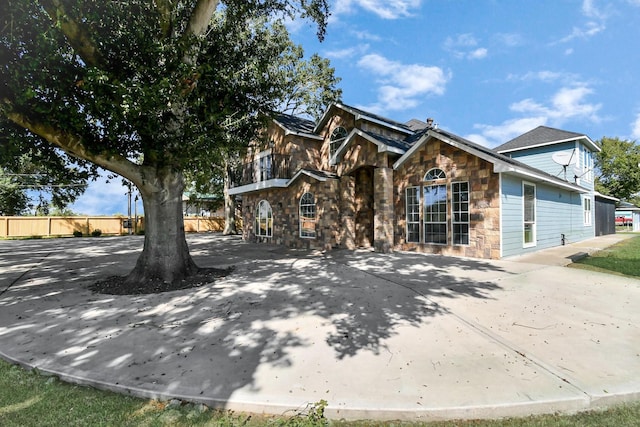 view of front of property featuring stone siding, fence, and driveway