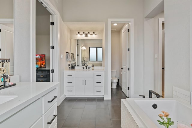 full bath with two vanities, a sink, tile patterned flooring, a relaxing tiled tub, and toilet