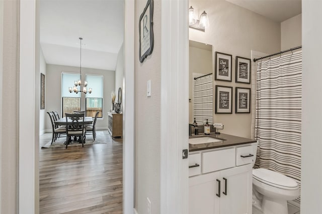 bathroom featuring vanity, wood finished floors, baseboards, an inviting chandelier, and toilet