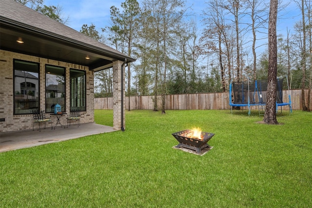 view of yard featuring a patio, a trampoline, a fenced backyard, and an outdoor fire pit