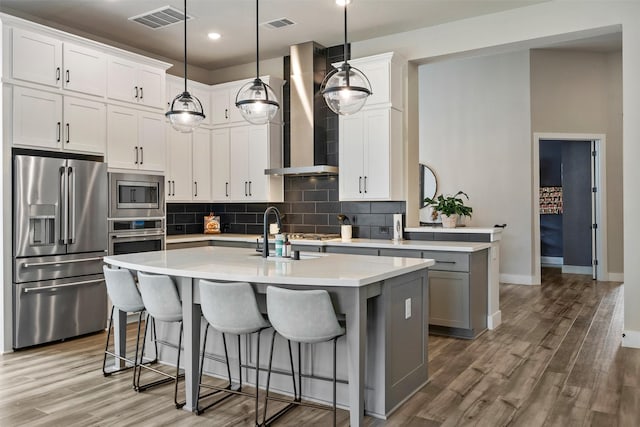 kitchen with visible vents, an island with sink, a sink, stainless steel appliances, and wall chimney exhaust hood