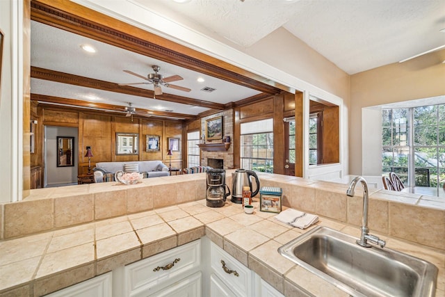 kitchen with beam ceiling, a fireplace, visible vents, white cabinetry, and a sink