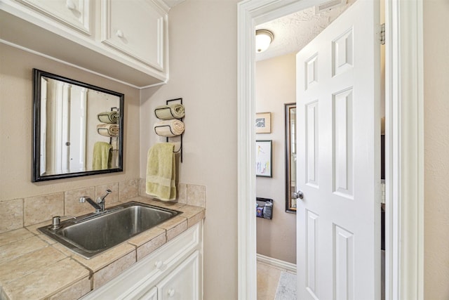 kitchen featuring tile countertops, white cabinetry, a sink, a textured ceiling, and baseboards