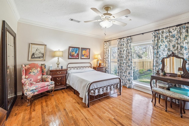 bedroom with ornamental molding, visible vents, a textured ceiling, and light wood finished floors