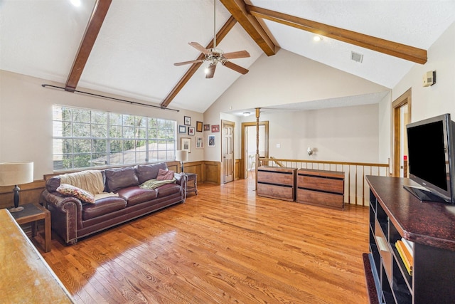 living area featuring high vaulted ceiling, light wood-style flooring, a wainscoted wall, visible vents, and beam ceiling