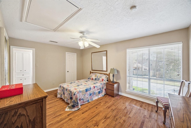 bedroom with attic access, baseboards, visible vents, wood finished floors, and a textured ceiling