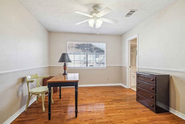 home office with a textured ceiling, light wood-type flooring, visible vents, and a ceiling fan